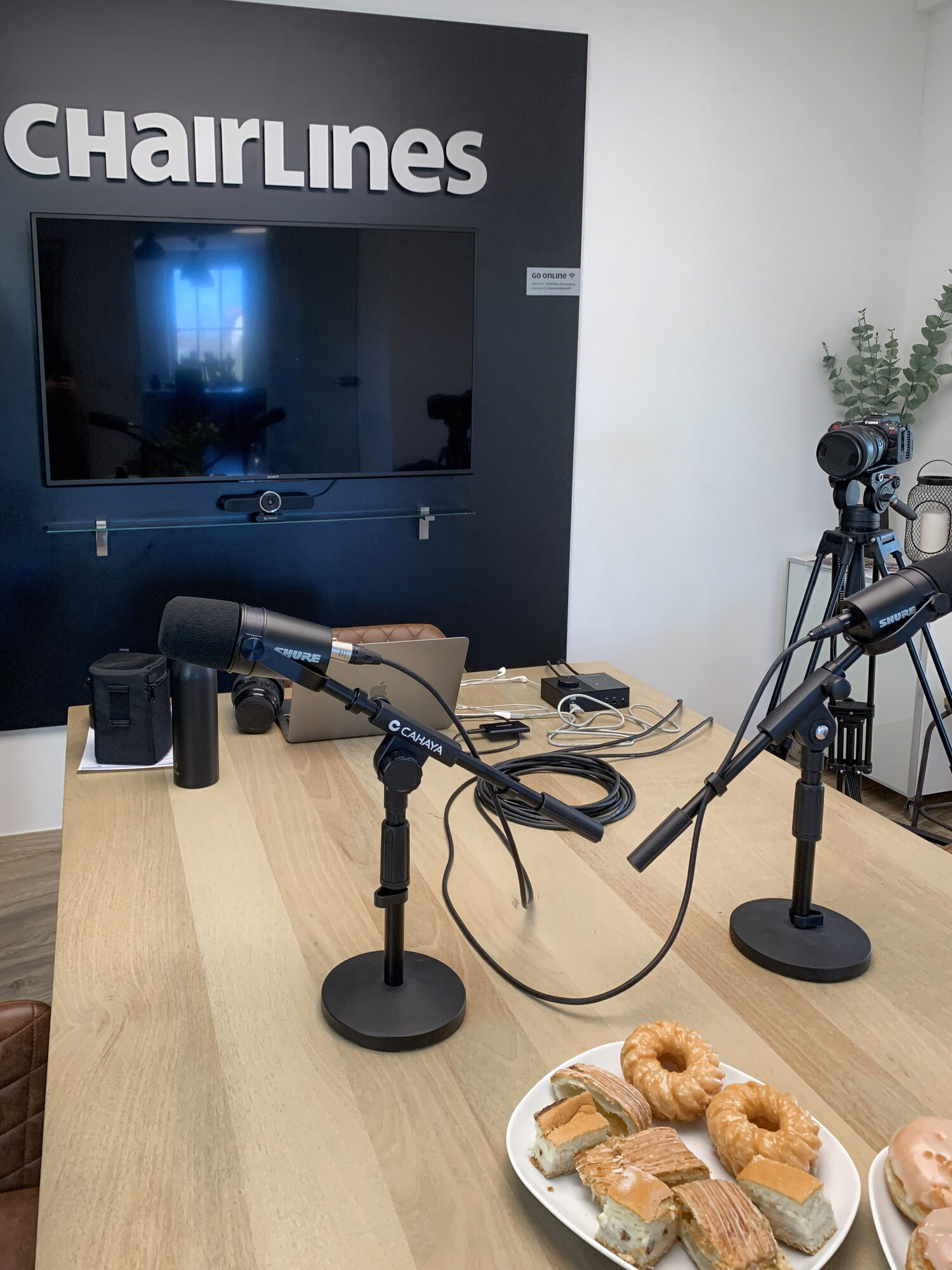 Zwei Mikrofone und Gebäck auf dem Tisch beim Podcast-Aufbau im Chairlines Studio